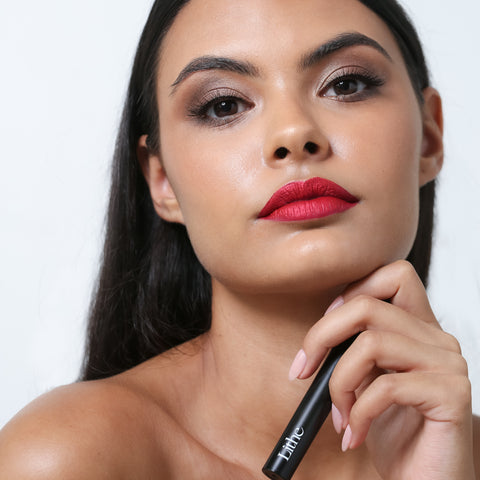Lithe Lashes false lashes accessories lash bond lash adhesive, waterproof and free of latex, parabens, phthalates, and formaldehyde. Lithe Lashes false lashes accessories lash bond lash adhesive, waterproof and free of latex, parabens, phthalates, and formaldehyde. The image shows a model holding the glue bottle in her left hand, showing the bottom half of the matte black bottle highlighting the Lithe logo on it.