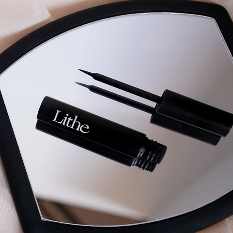 Lithe Lashes false lashes accessories lash bond lash adhesive, waterproof and free of latex, parabens, phthalates, and formaldehyde. The image shows the lash glue opened with the black bottle and ultra fine tip placed side by side on a diagonal pattern