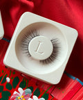 Lithe Lashes Mini Lashes lash style named M1 - Mini Round, a product image of the lashes in their biodegradable stowing tray, laying overtop red floral silk fabric.