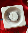 Lithe Lashes Mini Lashes lash style named M2 - Mini Winged, a product image of the lashes in their biodegradable stowing tray, laying overtop red floral silk fabric.