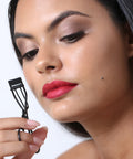 Lithe Lashes false lashes accessory, the Lithe Mini Lash Curler. An image of a model holding the matte black mini curler in her right hand, observing the sleek and sturdy feel of it in her hand.