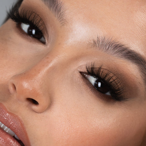 Lithe Lashes Bold Collection Style B4 - Wispy & Bold, an image of a model’s face wearing lithe lashes on both eyes, with full makeup, looking from a left side profile, semi zoomed in, displaying the elegance of the lashes on her eyes.